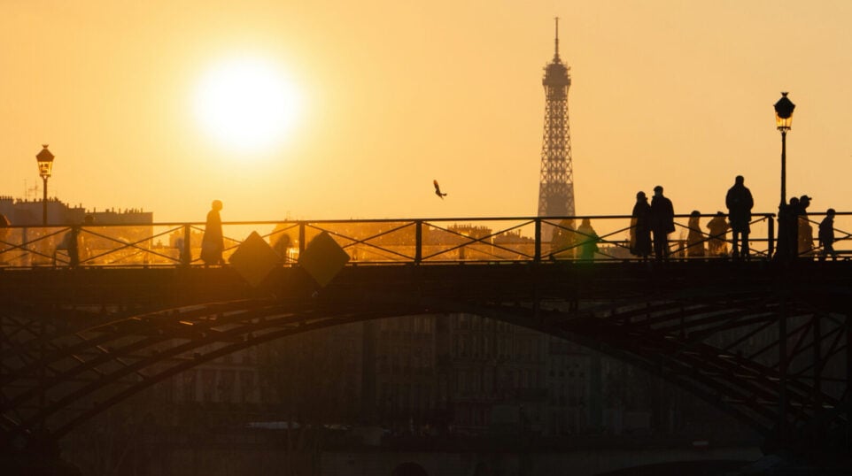 A goldent sunset with Eiffel tower in the background and pedestrians on a bridge in the forground